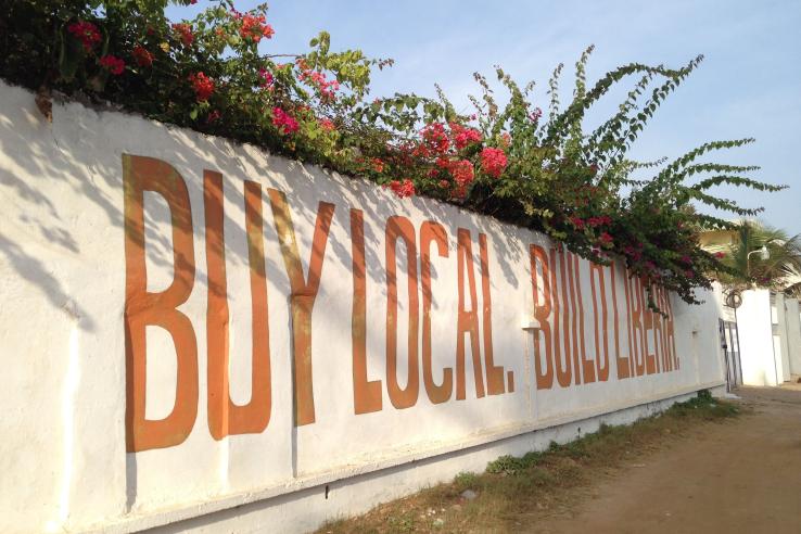 Street wall with words painted in orange reading "buy local build Liberia"