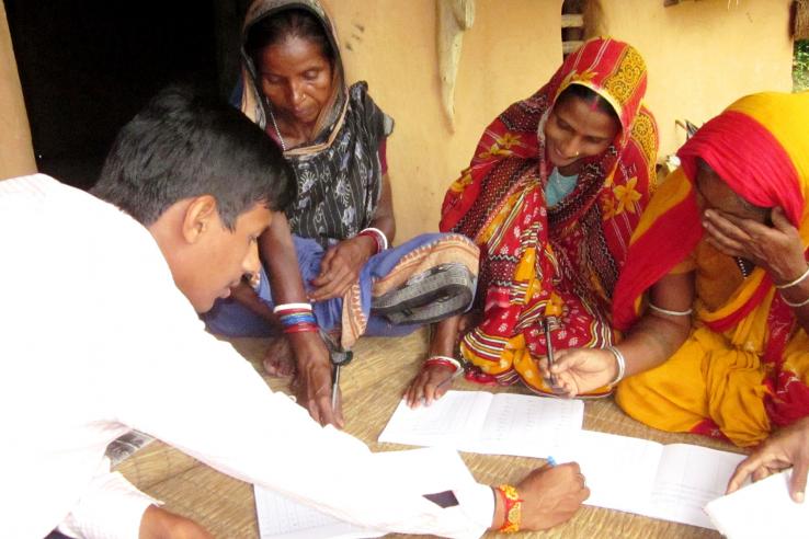 Three women in saris look at paperwork with Bandhan staff