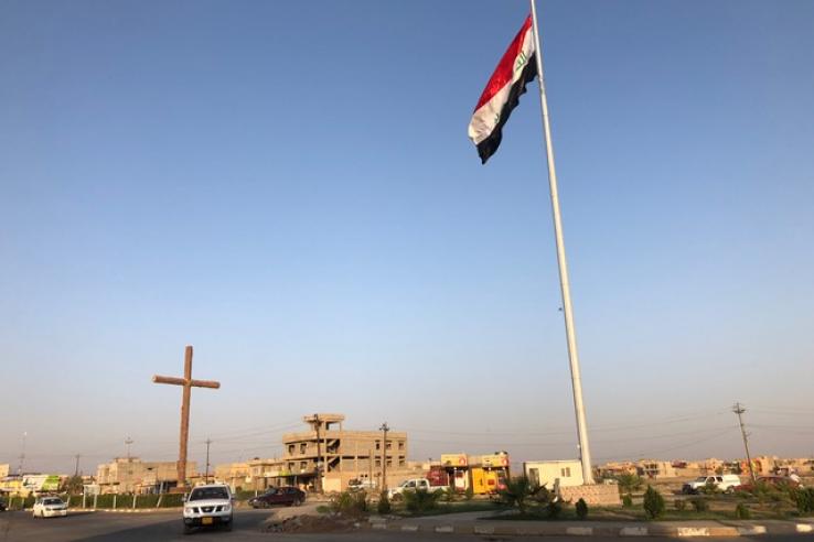 A car drives by a cross and Iraq's flag