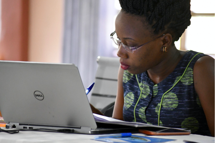 A woman works on her laptop in an office setting in Uganda.