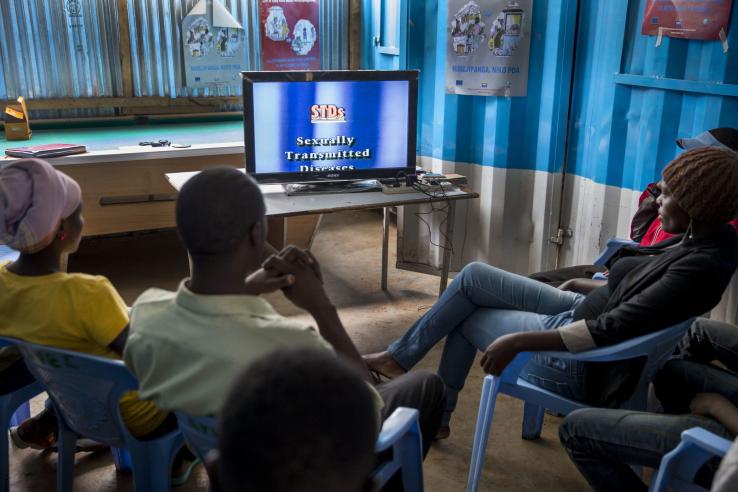 Several African young people sit in front of a television to watch an education program on sexually transmitted diseases.