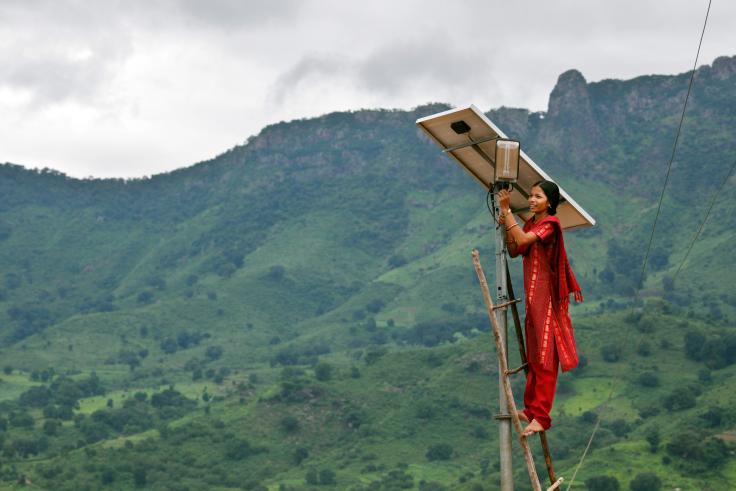 A woman cleans a solar panel, mountains in the background.