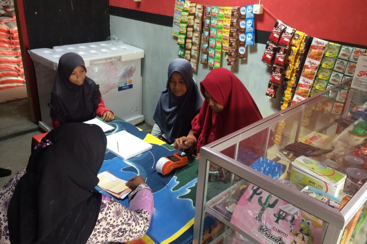 Four women group around a counter at a small shop. One woman is performing a transaction on a digital card reader.